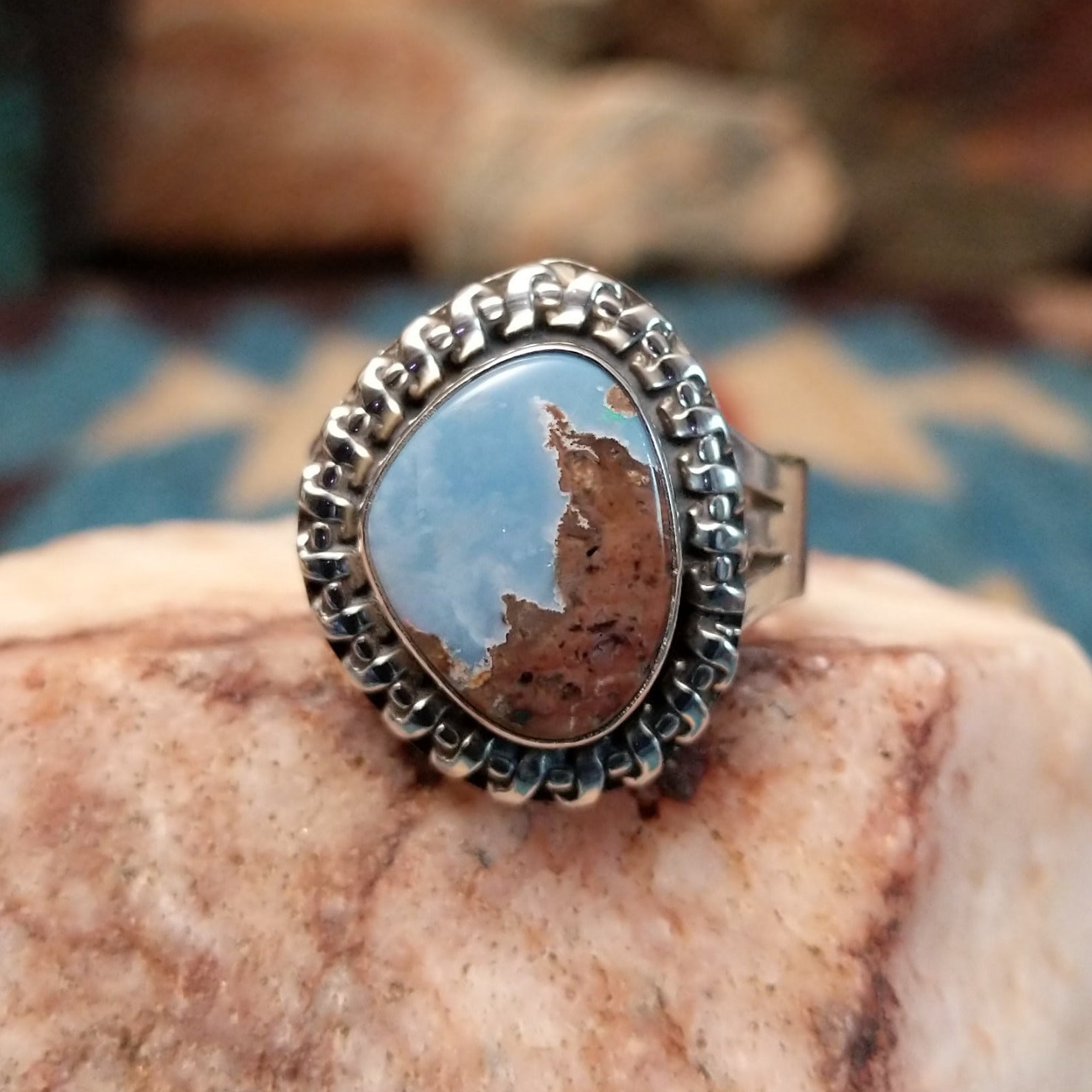 Sterling silver ring with Arizona blue opal set in the bezel, framed by the ornate setting and features vibrant green and red firing.