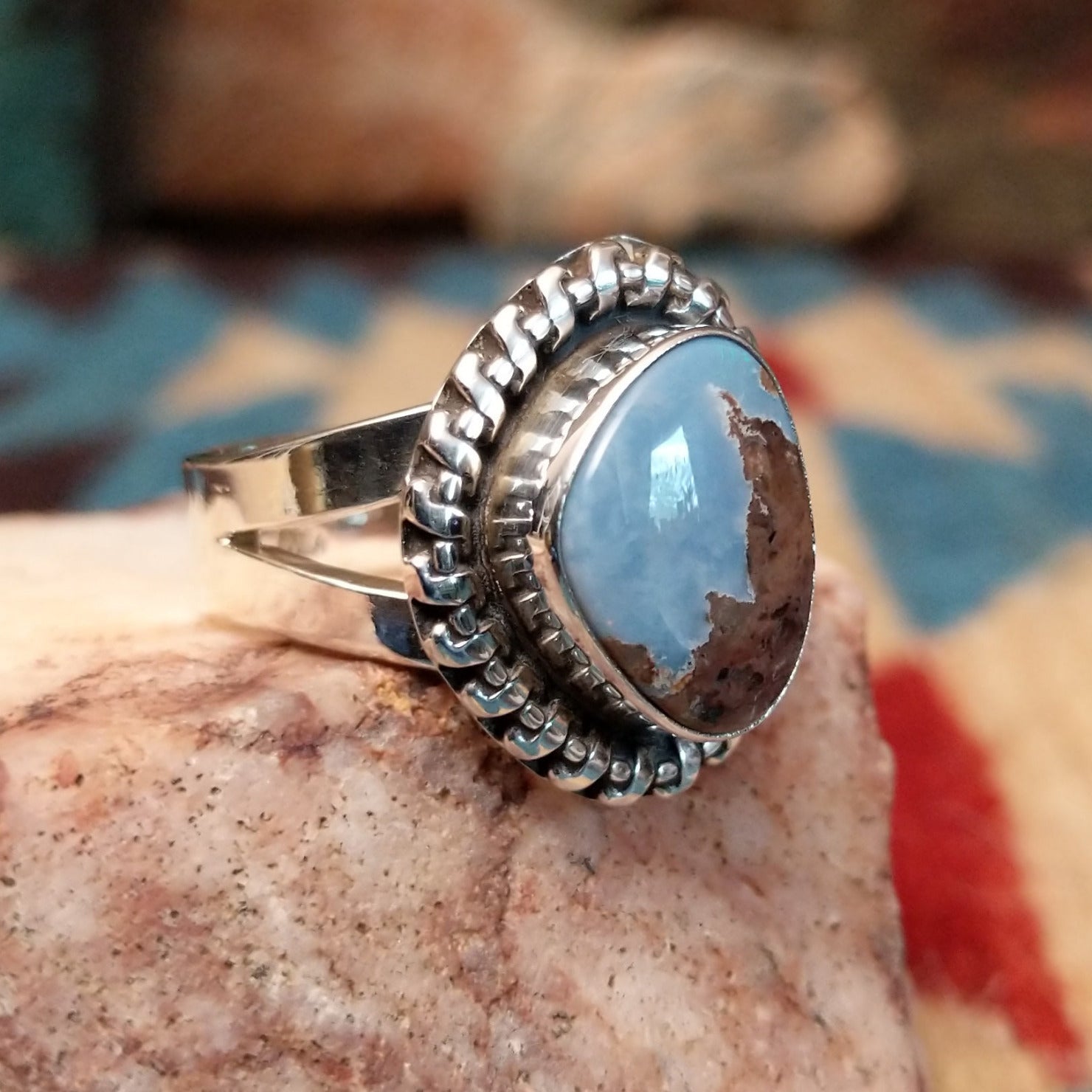 Sterling silver ring with Arizona blue opal set in the bezel, framed by the ornate setting and features vibrant green and red firing.