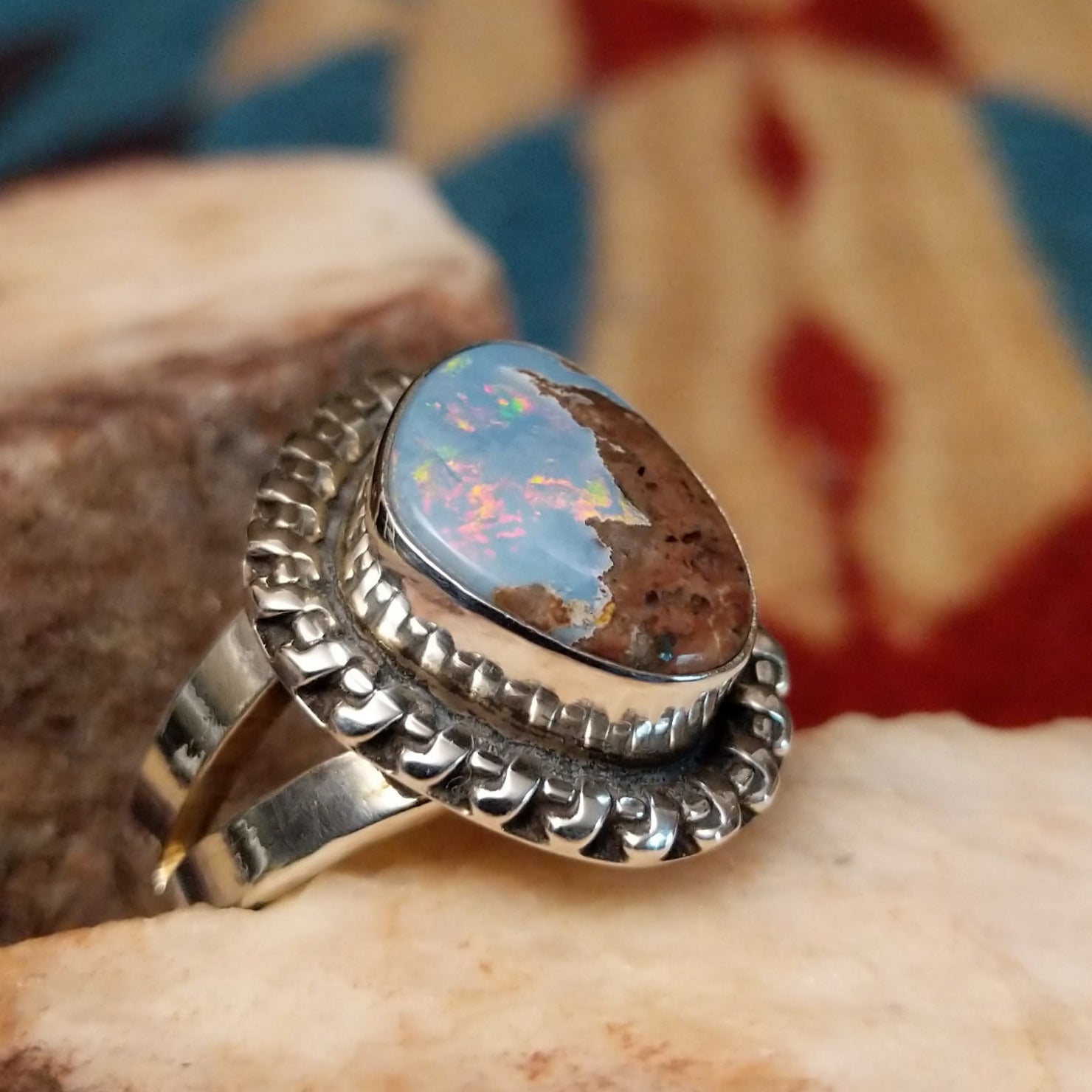 Sterling silver ring with Arizona blue opal set in the bezel, framed by the ornate setting and features vibrant green and red firing.