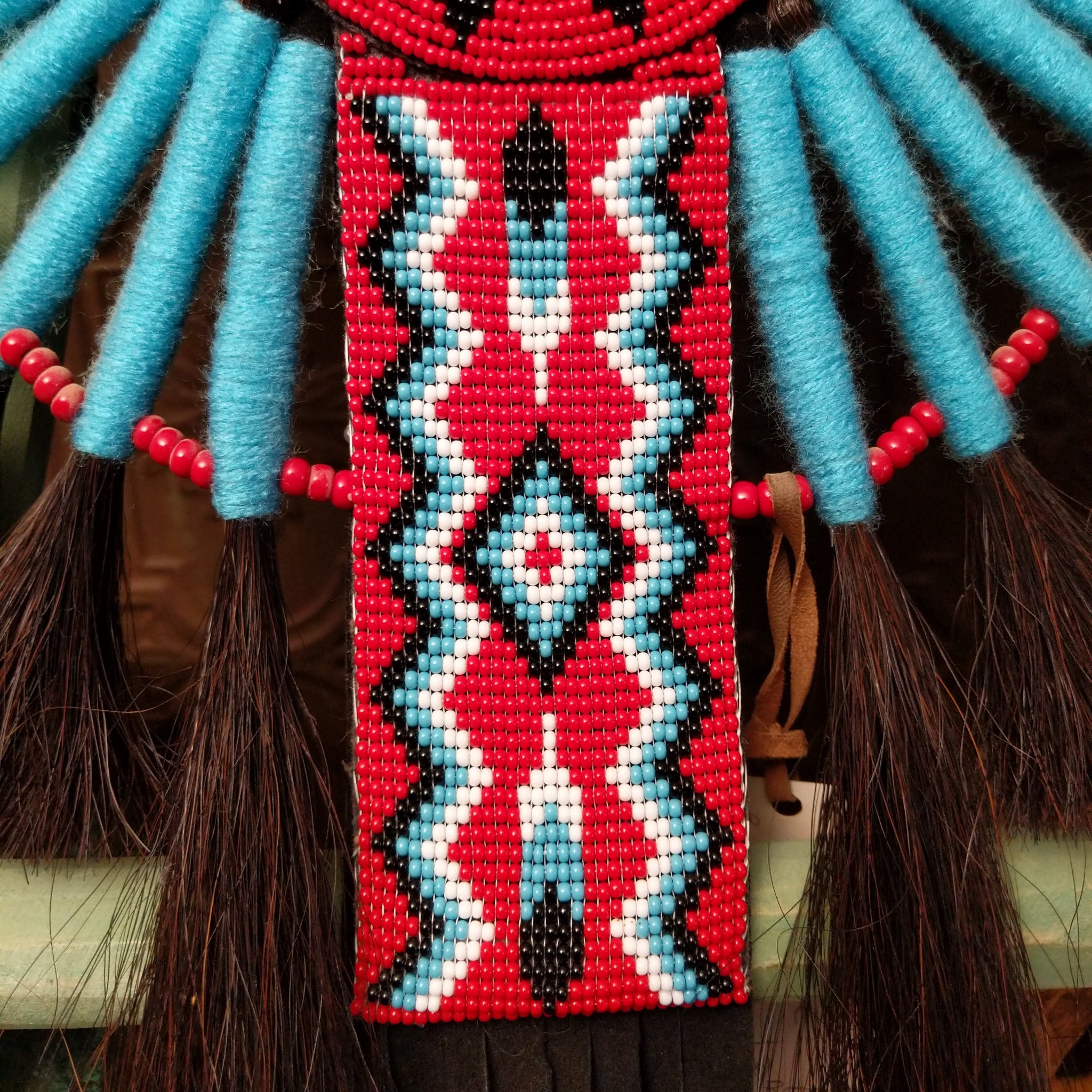 Blue Navajo Bustle artifact reproduction by Linda Lee with beadwork by Dorothy Manning, featuring turquoise, red, black, and white beadwork with dark horsehair accents.
