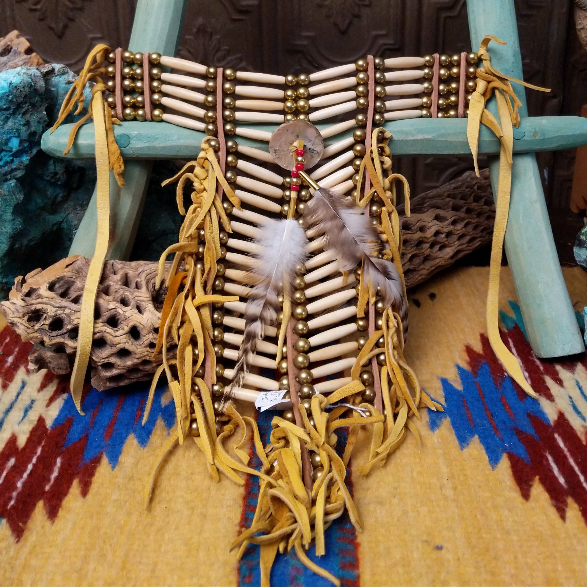 Breastplate artifact reproduction by Linda Lee featuring bone hairpipe beads, leather fringe, brass-toned beads, and feather accents.