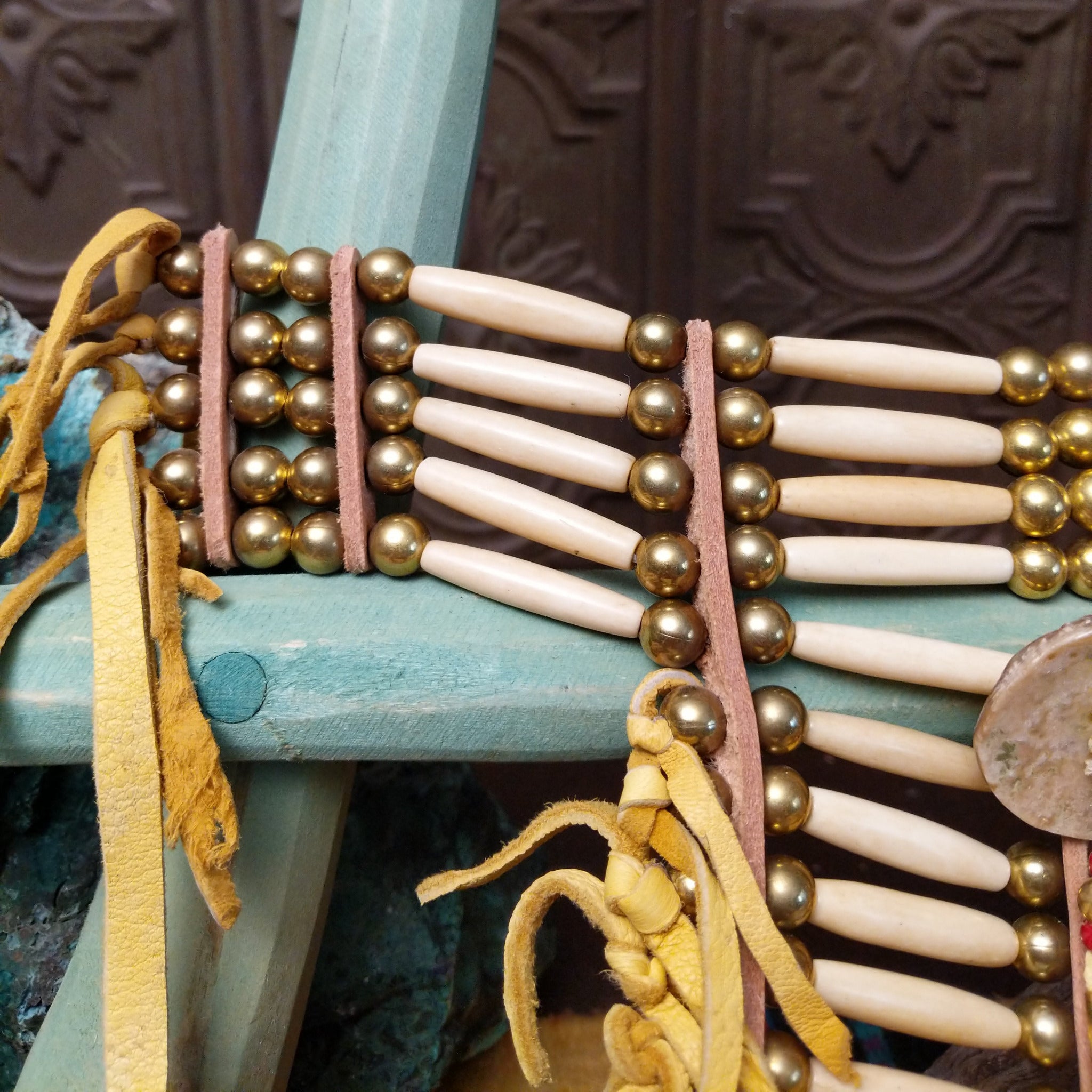 Breastplate artifact reproduction by Linda Lee featuring bone hairpipe beads, leather fringe, brass-toned beads, and feather accents.
