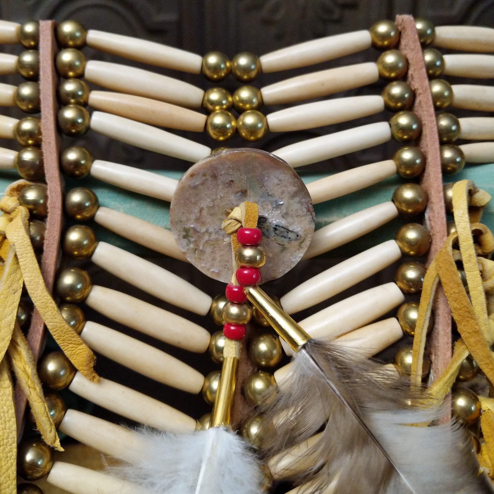 Breastplate artifact reproduction by Linda Lee featuring bone hairpipe beads, leather fringe, brass-toned beads, and feather accents.