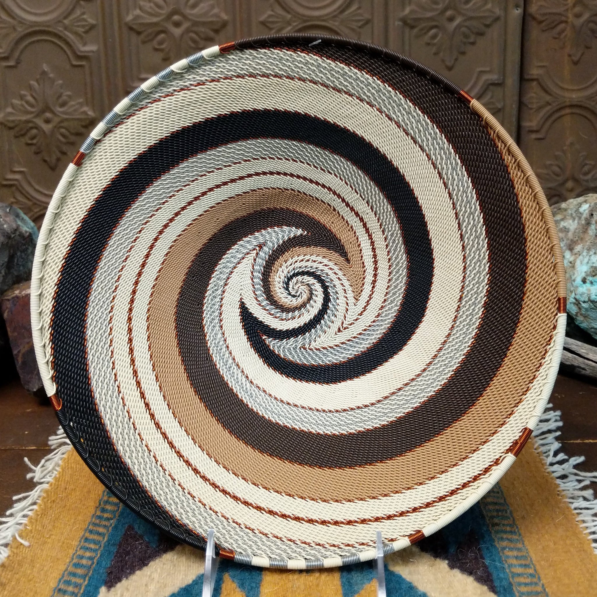 Handwoven large earth tone wire art bowl by Bridge for Africa featuring a spiral pattern in recycled wire with ivory, beige, taupe, gray, brown, and black tones, perfect for home décor or wall display.