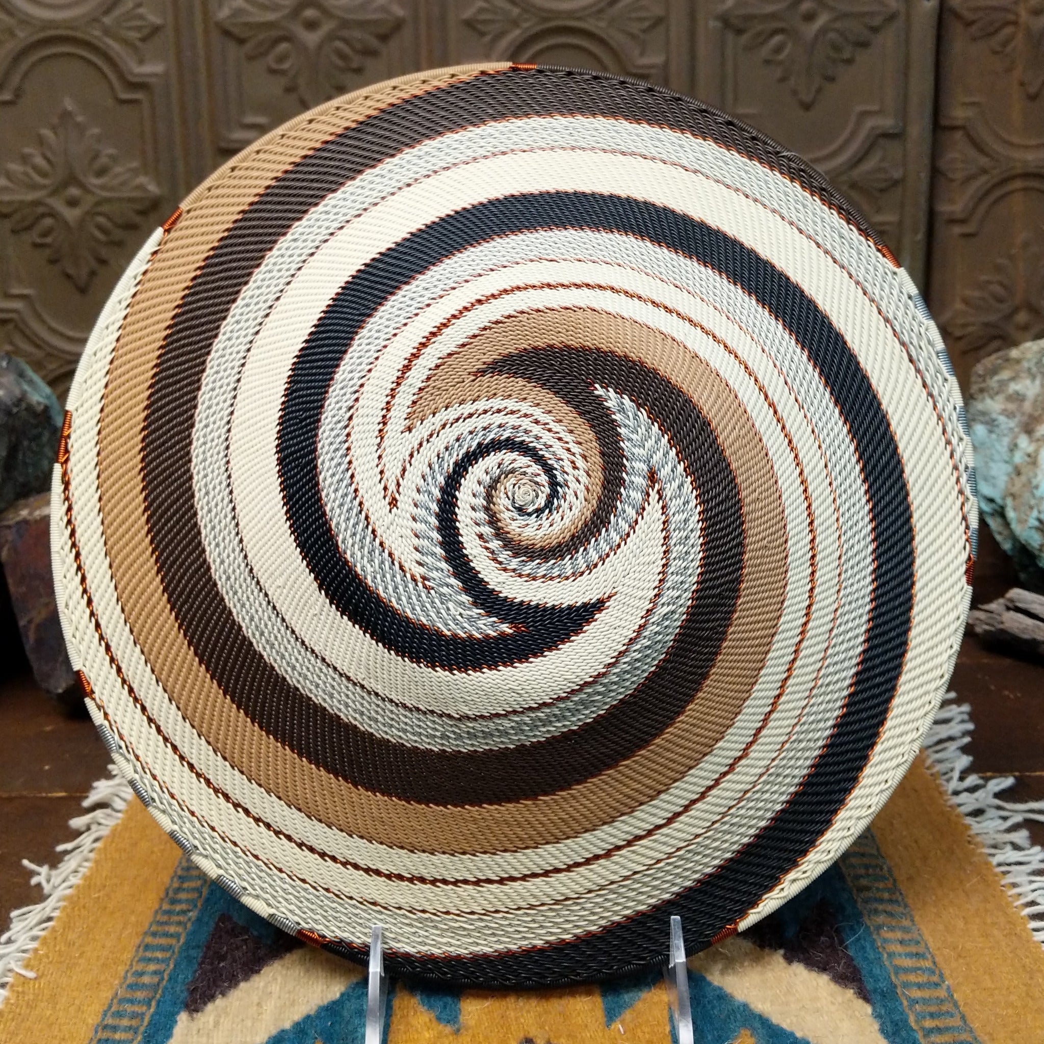 Handwoven large earth tone wire art bowl by Bridge for Africa featuring a spiral pattern in recycled wire with ivory, beige, taupe, gray, brown, and black tones, perfect for home décor or wall display; underside view.