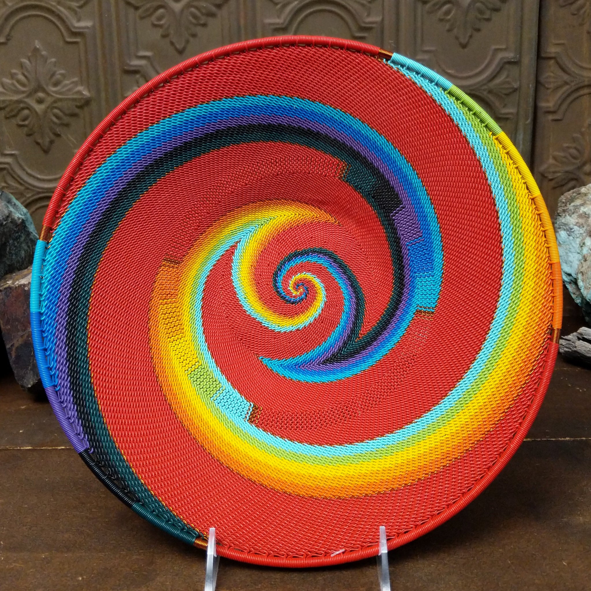 Handwoven large multicolor wire art basket by Bridge for Africa featuring a vibrant spiral pattern in recycled wire with bold red, blue, turquoise, green, yellow, orange, purple, and black accents.