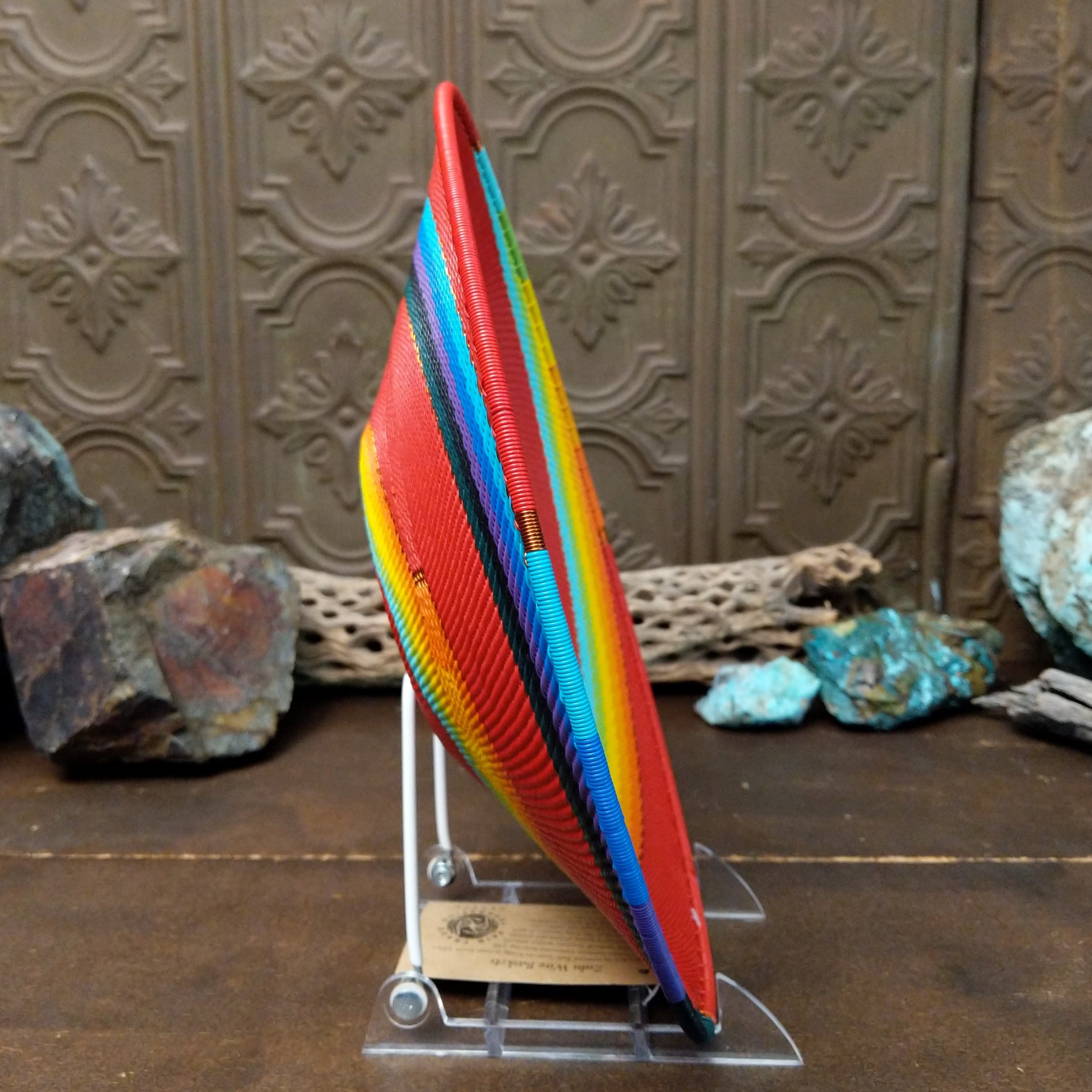 Handwoven large multicolor wire art basket by Bridge for Africa featuring a vibrant spiral pattern in recycled wire with bold red, blue, turquoise, green, yellow, orange, purple, and black accents; side view.