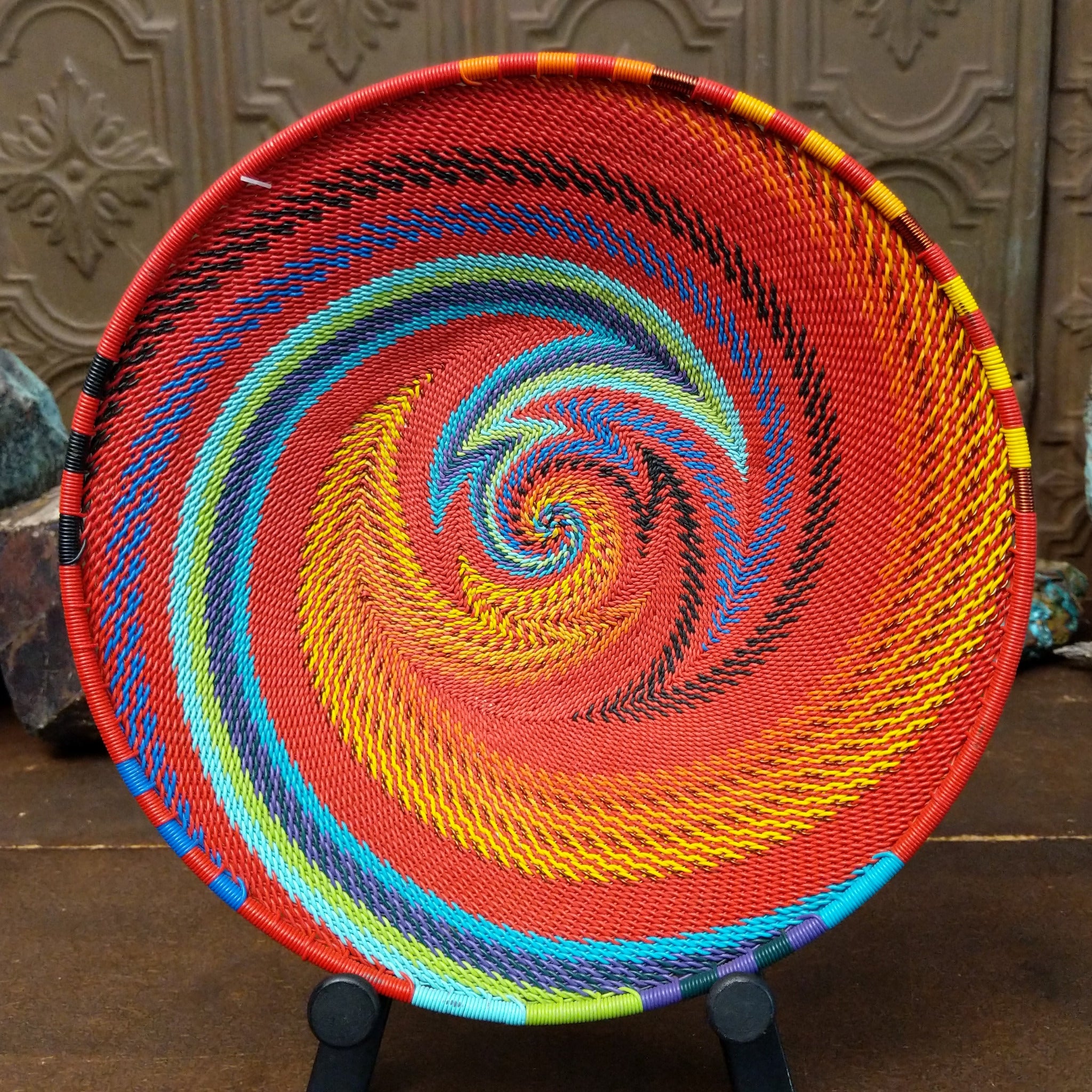 Handwoven multicolor wire art basket by Bridge for Africa featuring a vibrant spiral pattern made from recycled wire in bold rainbow colors, ideal for display or home décor.