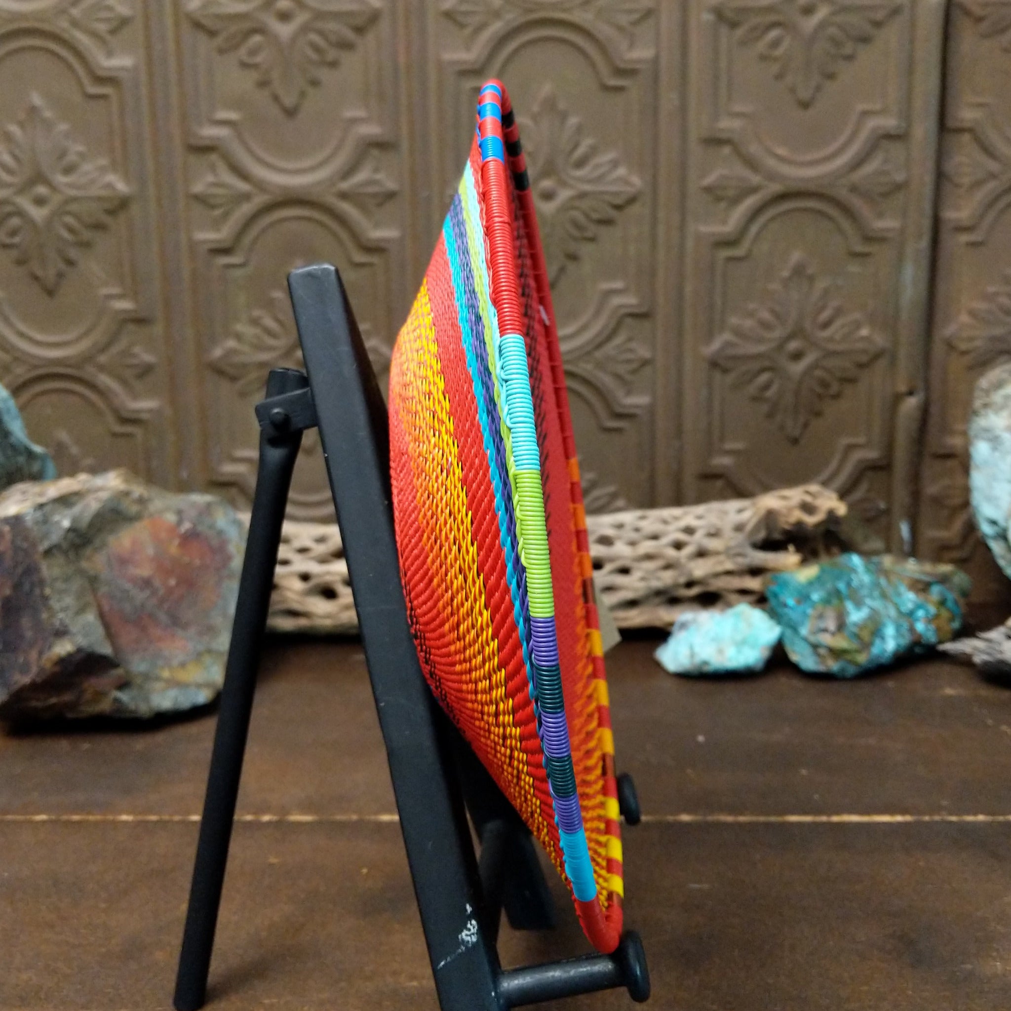 Handwoven multicolor wire art basket by Bridge for Africa featuring a vibrant spiral pattern made from recycled wire in bold rainbow colors, ideal for display or home décor; side view.
