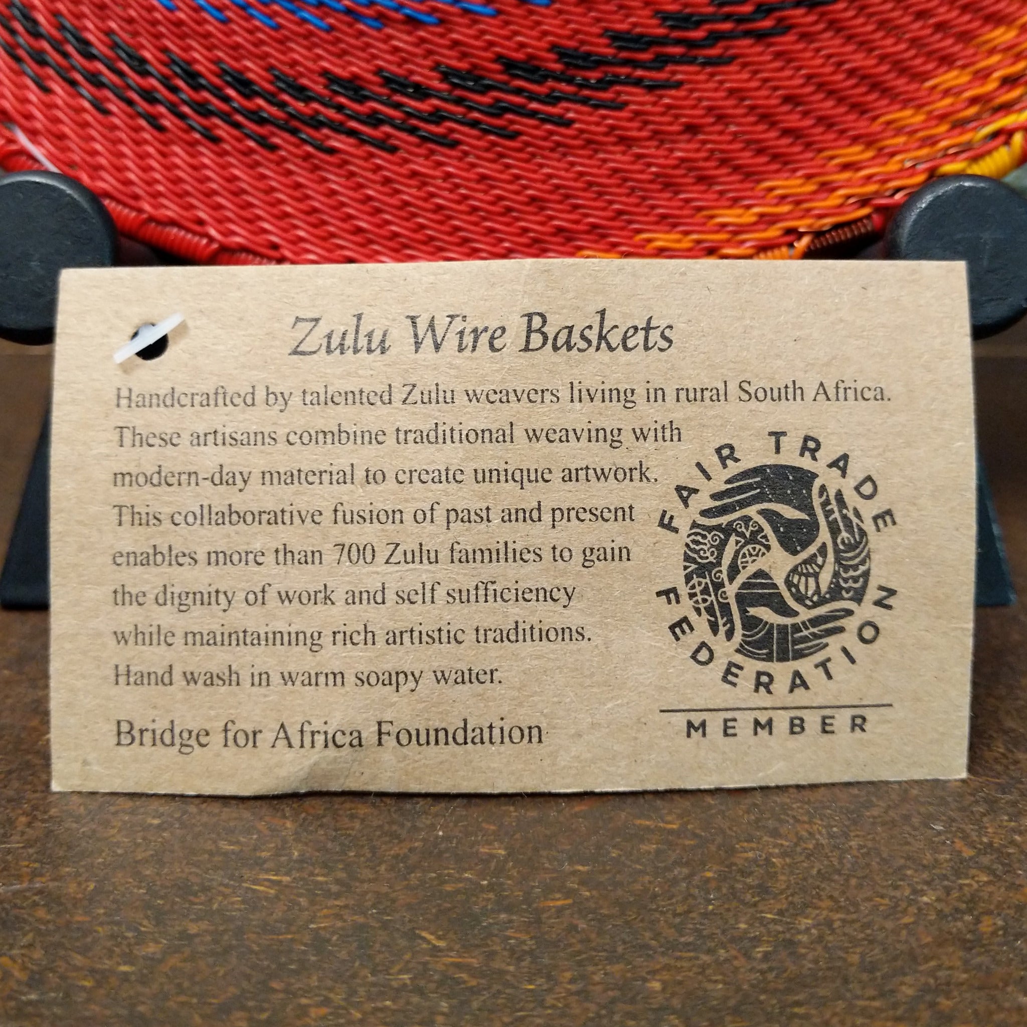 Handwoven multicolor wire art basket by Bridge for Africa featuring a vibrant spiral pattern made from recycled wire in bold rainbow colors, ideal for display or home décor; artisan information.