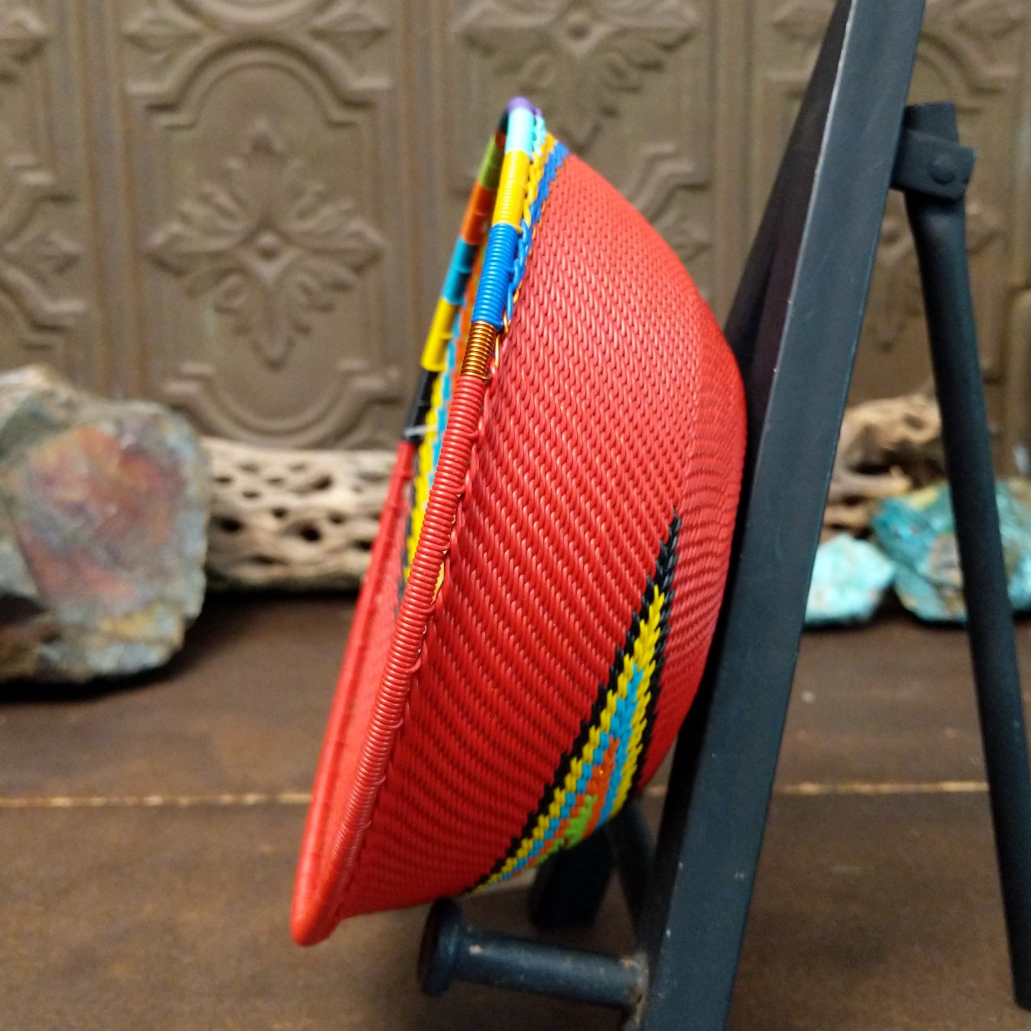 Handwoven multicolor wire art bowl by Bridge for Africa featuring a vibrant spiral design made from recycled wire in bold red, blue, green, yellow, orange, purple, and black tones; side view.