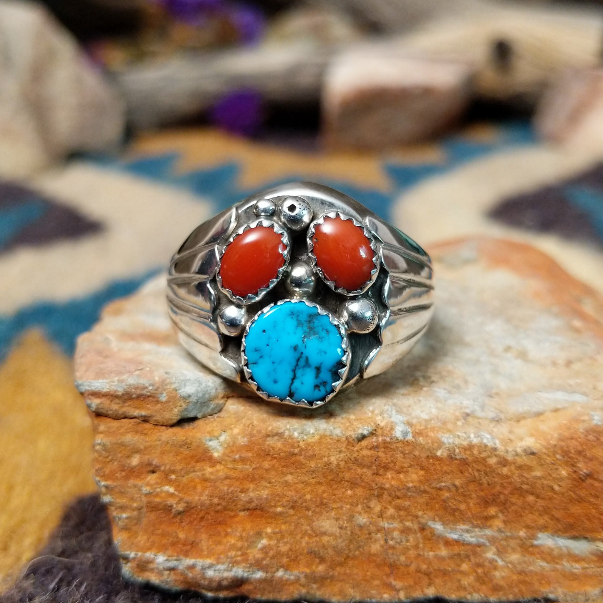 Handcrafted Navajo sterling silver ring featuring two natural red coral cabochons and one blue turquoise cabochon with traditional sawtooth bezels, silver raindrop accents, and a split-shank band.