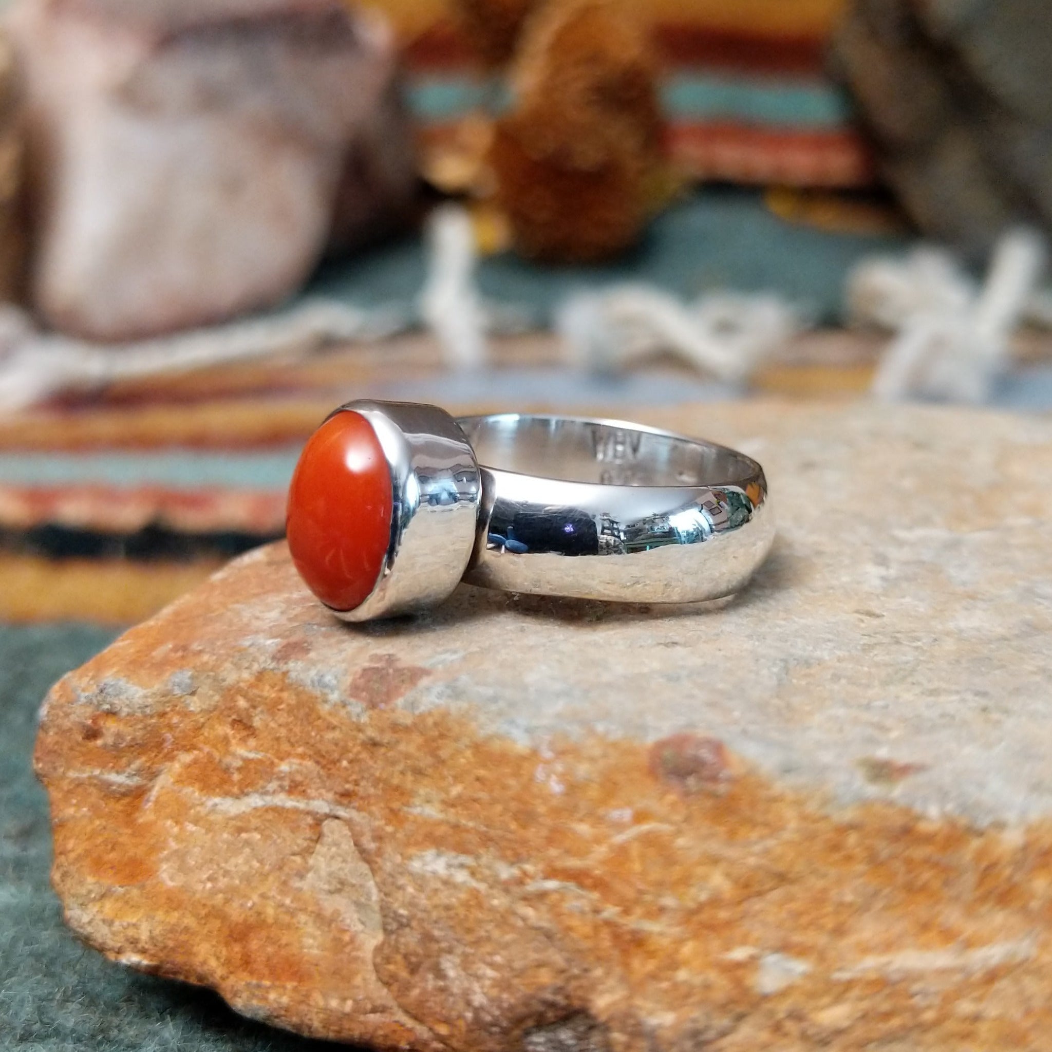 Navajo sterling silver ring by W.B.V. featuring a smooth oval red coral cabochon set in a polished silver bezel and band; side view.