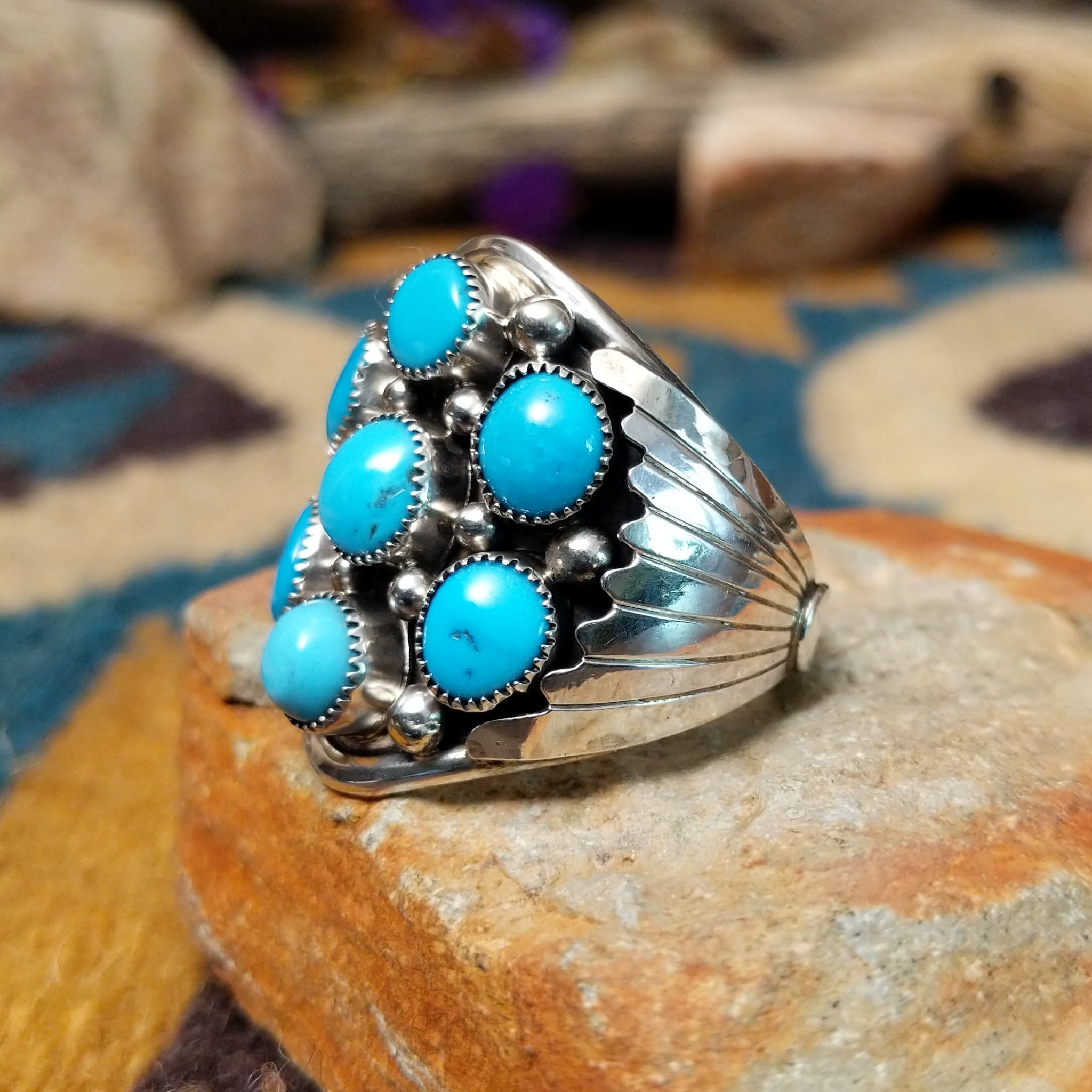 Sterling silver Navajo turquoise cluster ring featuring seven turquoise cabochons, serrated bezels, silver raindrop accents, and a classic Southwestern floral cluster design; side view.
