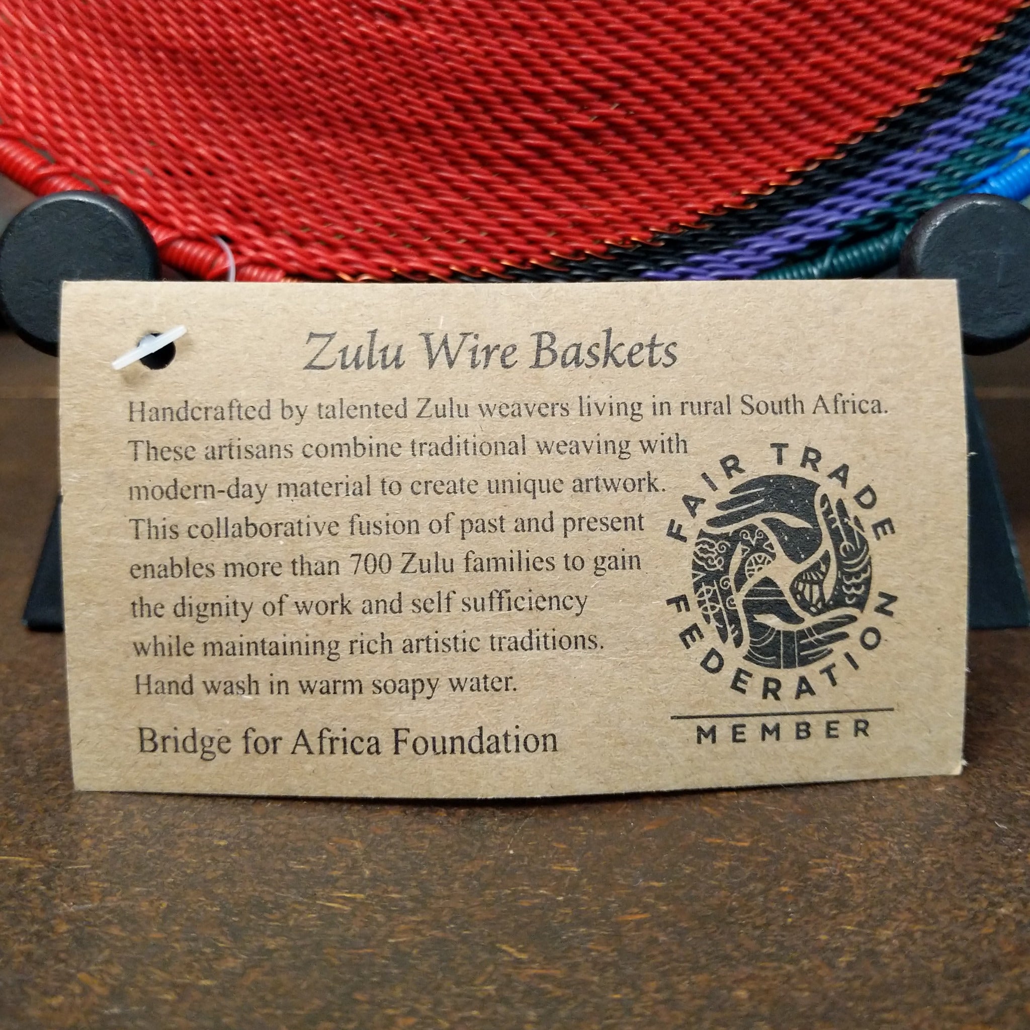Handwoven rainbow wire art basket by Bridge for Africa featuring colorful recycled wire in a vibrant geometric pattern, ideal as a decorative bowl or wall display; artisan information.