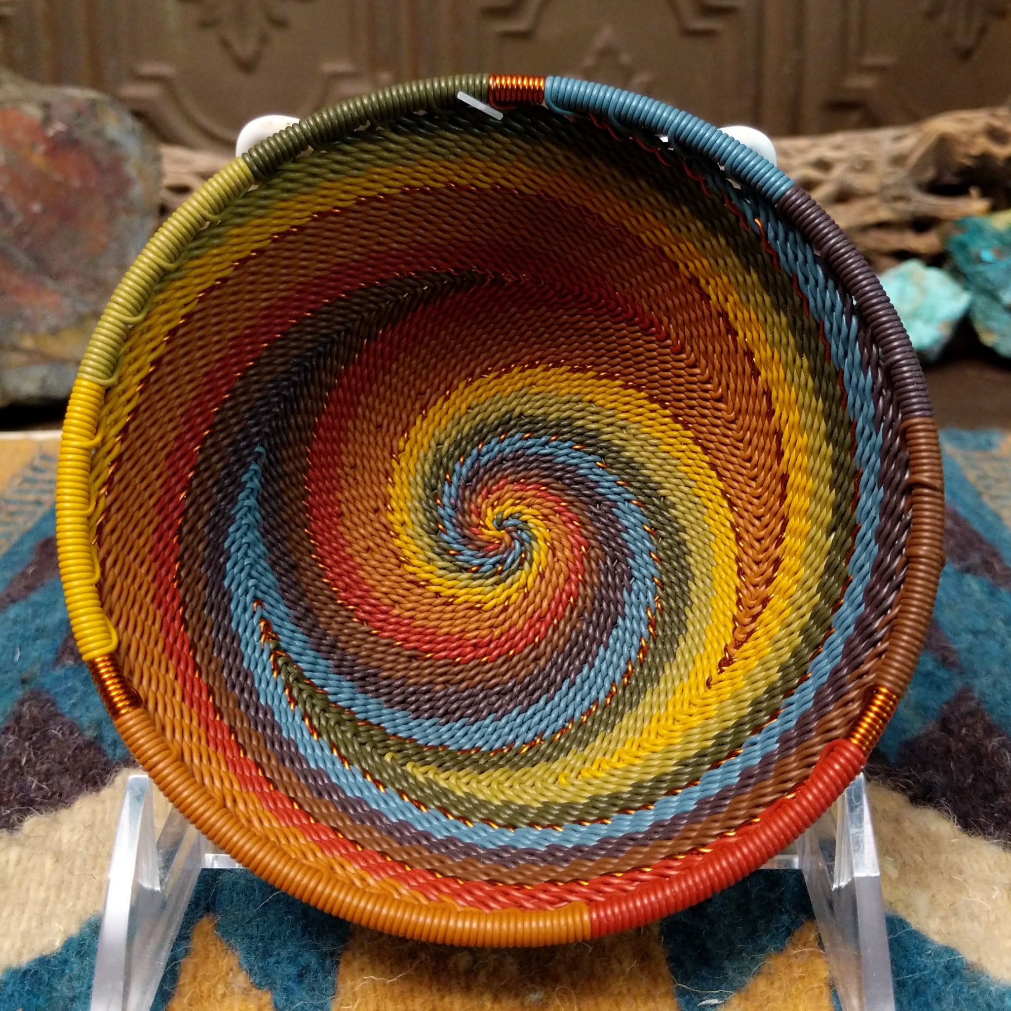 Handwoven small wire art bowl by Bridge for Africa featuring a spiral pattern in recycled wire with mustard yellow, olive green, dusty blue, rust, terracotta, brown, and charcoal tones, ideal for home décor or as a decorative catchall.