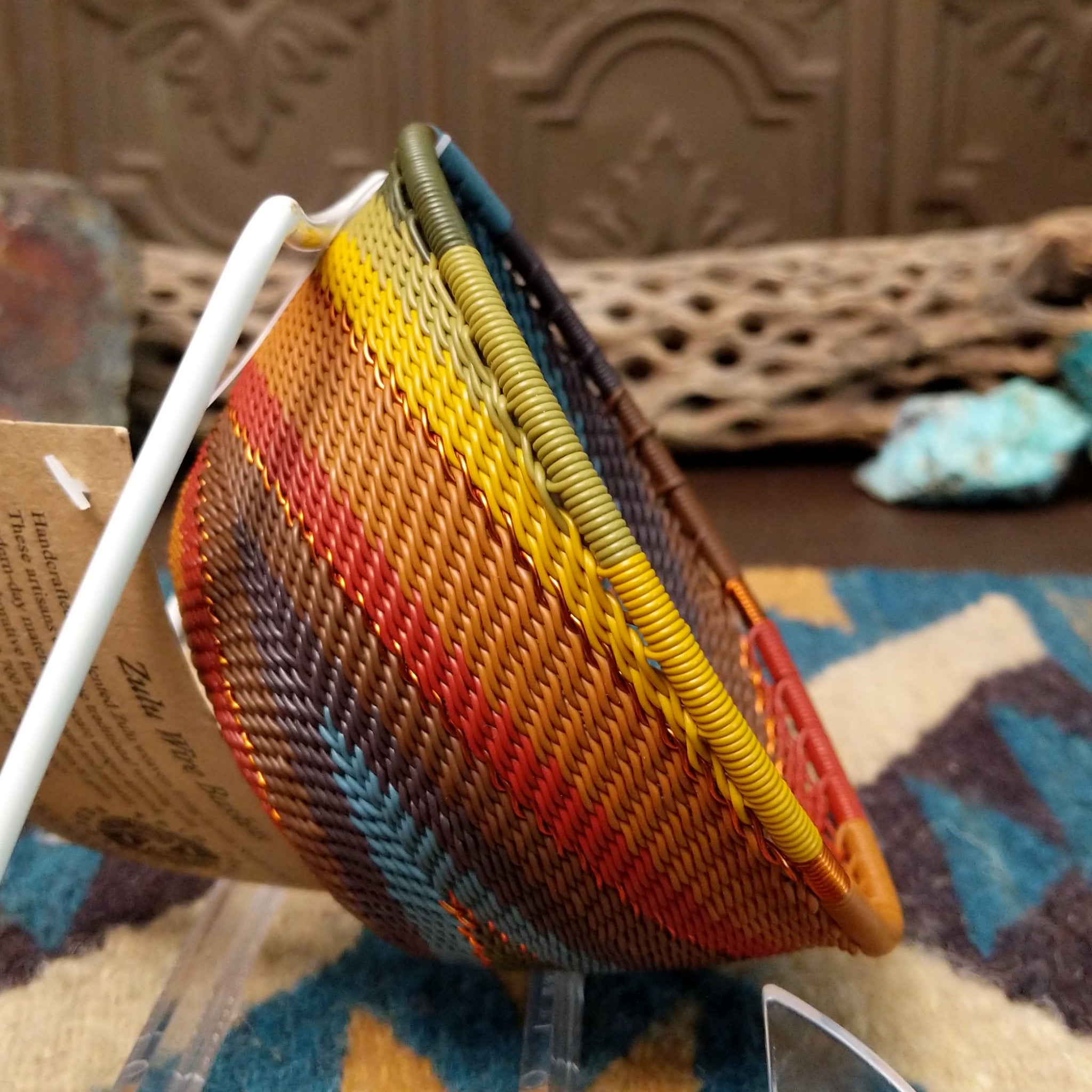 Handwoven small wire art bowl by Bridge for Africa featuring a spiral pattern in recycled wire with mustard yellow, olive green, dusty blue, rust, terracotta, brown, and charcoal tones, ideal for home décor or as a decorative catchall; side view.
