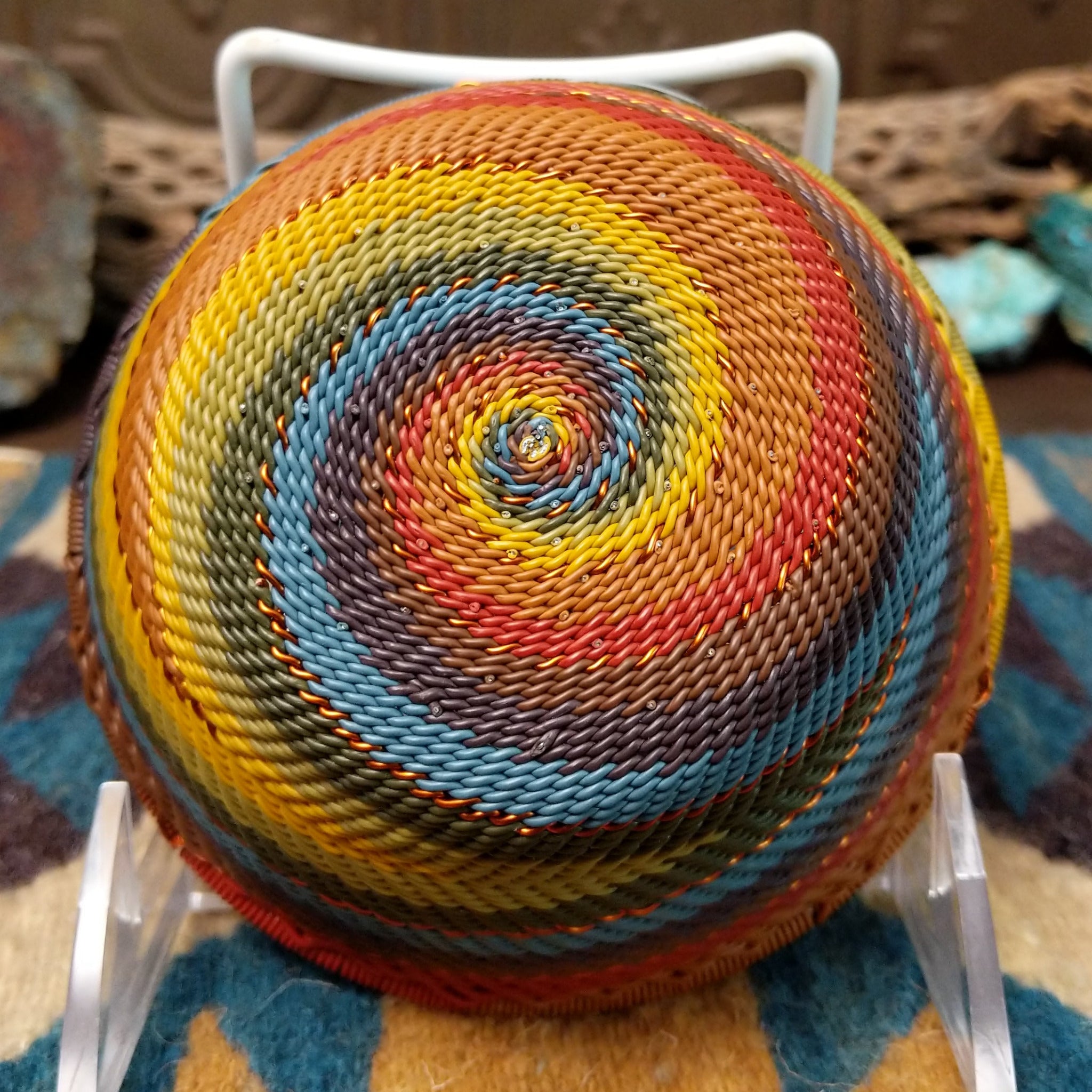 Handwoven small wire art bowl by Bridge for Africa featuring a spiral pattern in recycled wire with mustard yellow, olive green, dusty blue, rust, terracotta, brown, and charcoal tones, ideal for home décor or as a decorative catchall; underside view.
