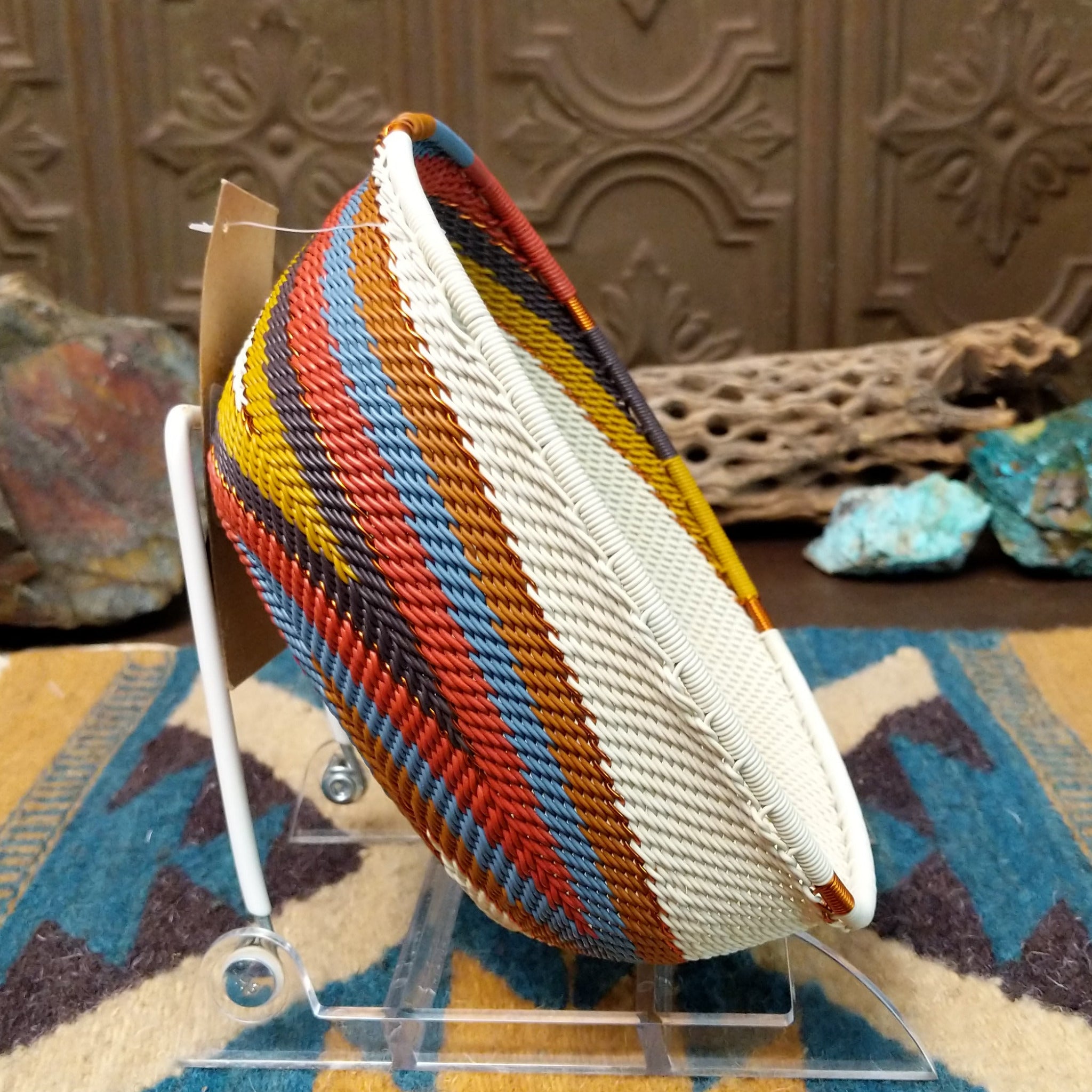 Handwoven square wire art bowl by Bridge for Africa featuring a spiral pattern in recycled wire with ivory, rust, blue, gold, brown, and charcoal tones, ideal for home décor or wall display; side view.