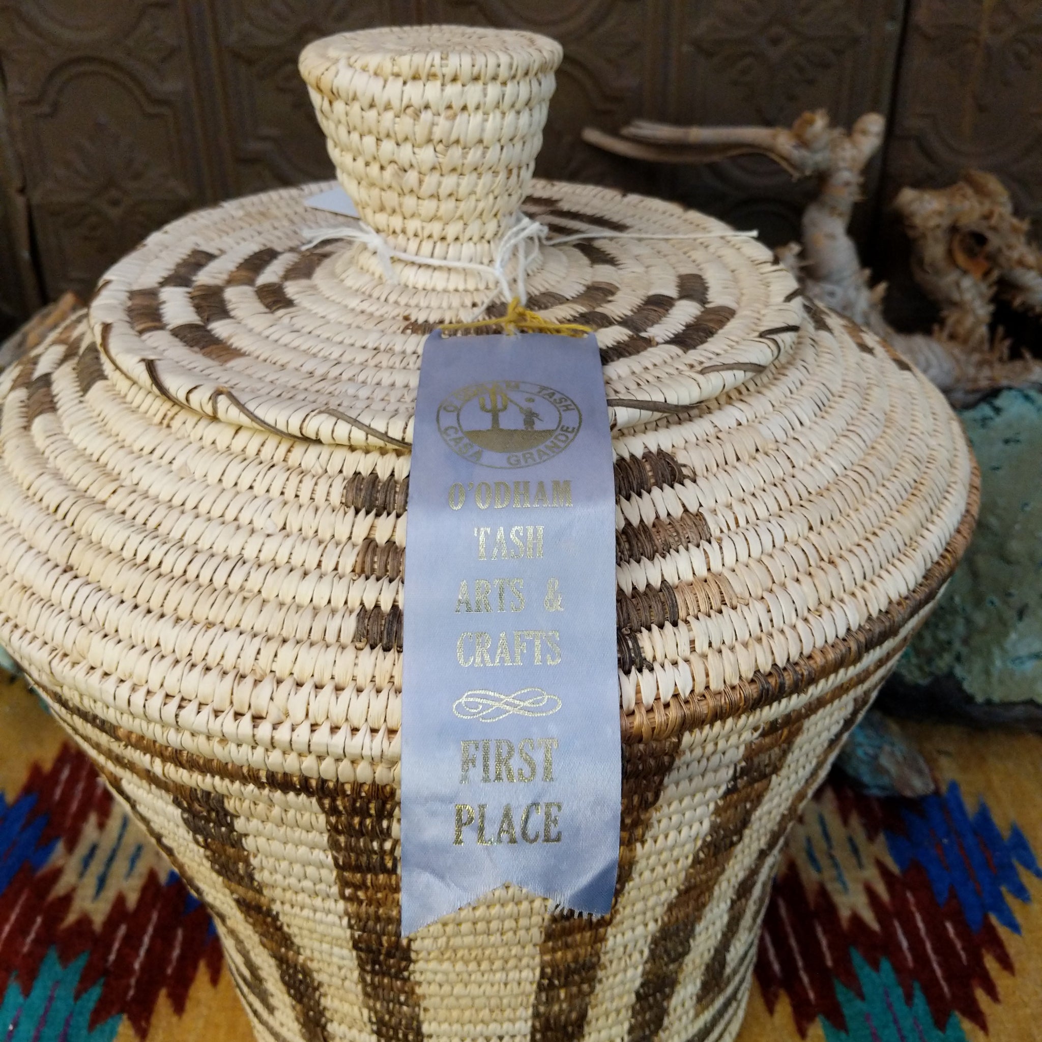 Award-winning Tohono O'odham handwoven lidded basket by Mary Thomas with geometric woven patterns in natural and dark fibers.