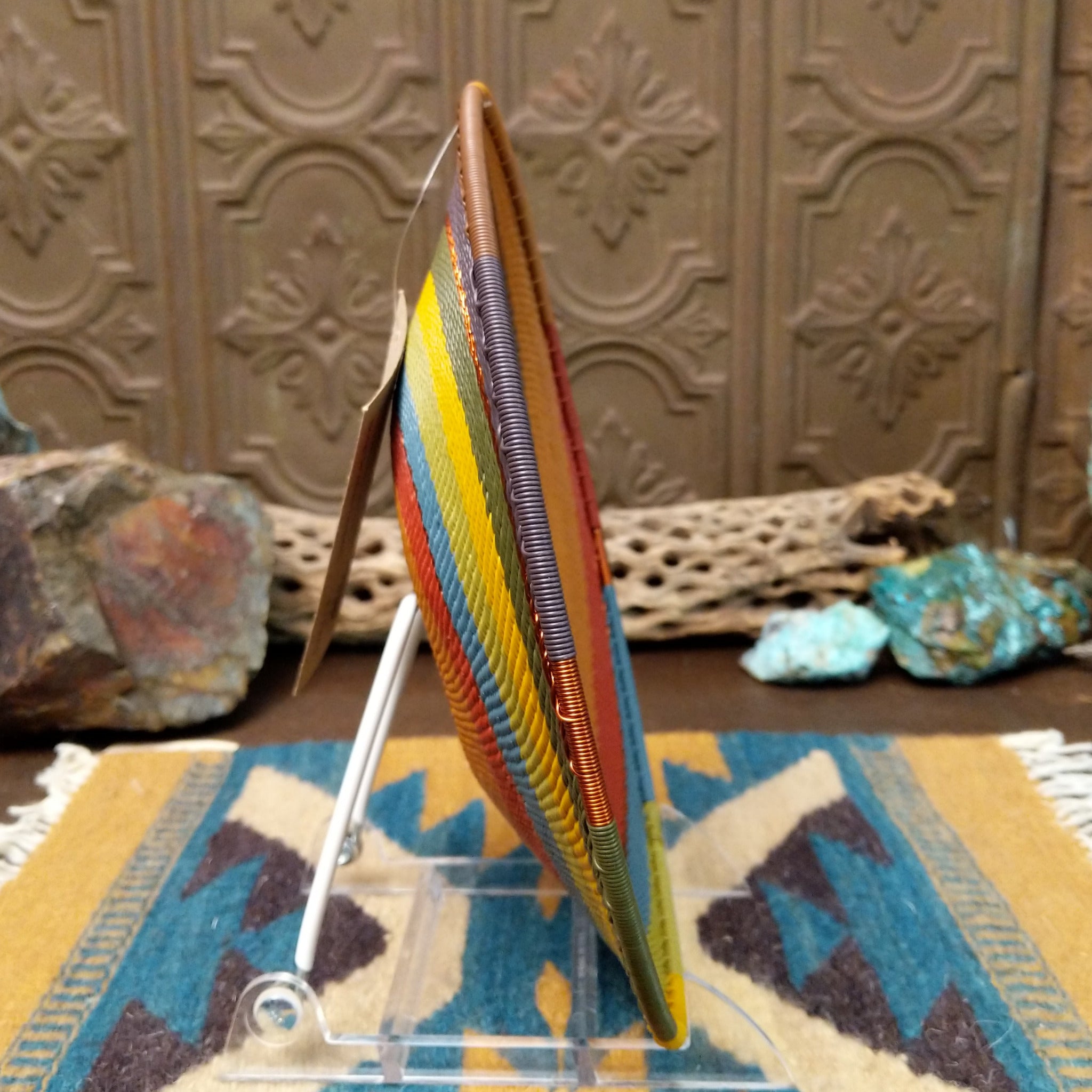 Handwoven wire art bowl by Bridge for Africa featuring a spiral pattern in recycled wire with golden yellow, olive green, dusty blue, rust, tan, brown, and charcoal tones, ideal for home décor or wall display; side view.